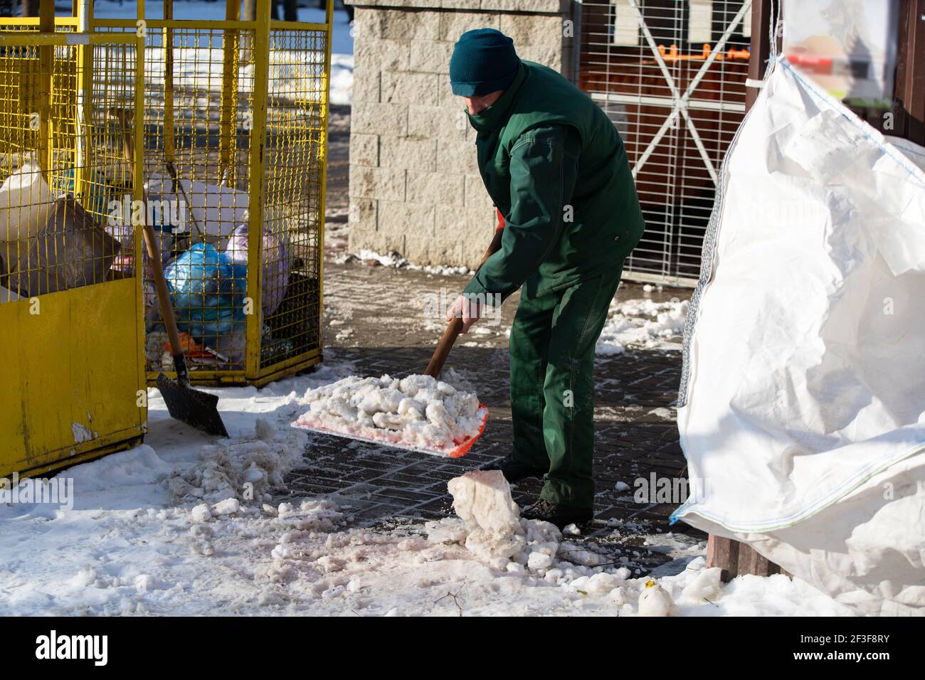A manual worker scoops snow from the pavement and shovels it onto a ...