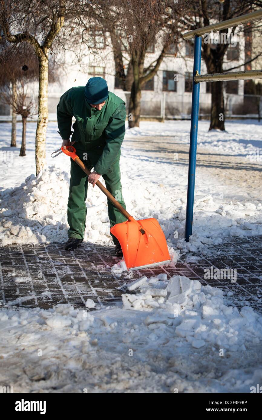 The landlord scrapes snow and ice with an orange cobblestone shovel Stock Photo