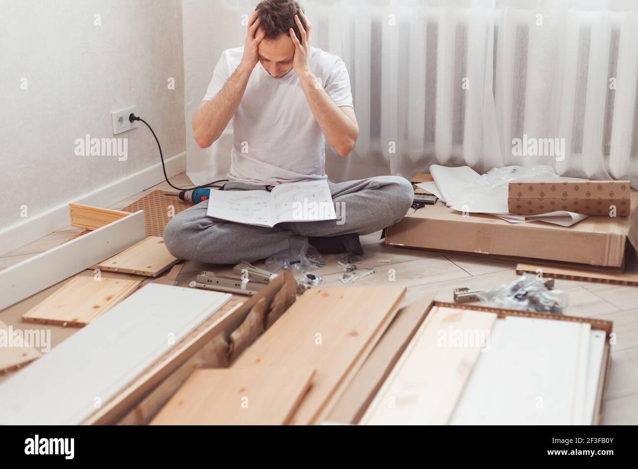 Bewildered man assembling new wooden furniture at home. Man reading instructions and misunderstand what to do the next. Stock Photo