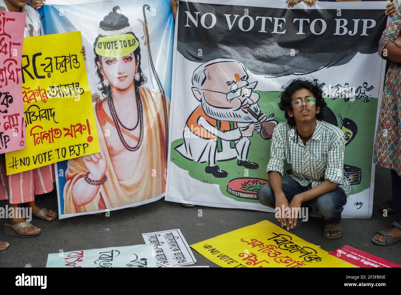 A student activist sits in front of a banner printed with image of lord Rama and 'No Vote to BJP (Bhartiya janta Party)' during a demonstration staged by students in protest against BJP (Bhartiya Janta Party) and to promote 'No Vote to BJP' movement prior to West Bengal assembly elections. Stock Photo
