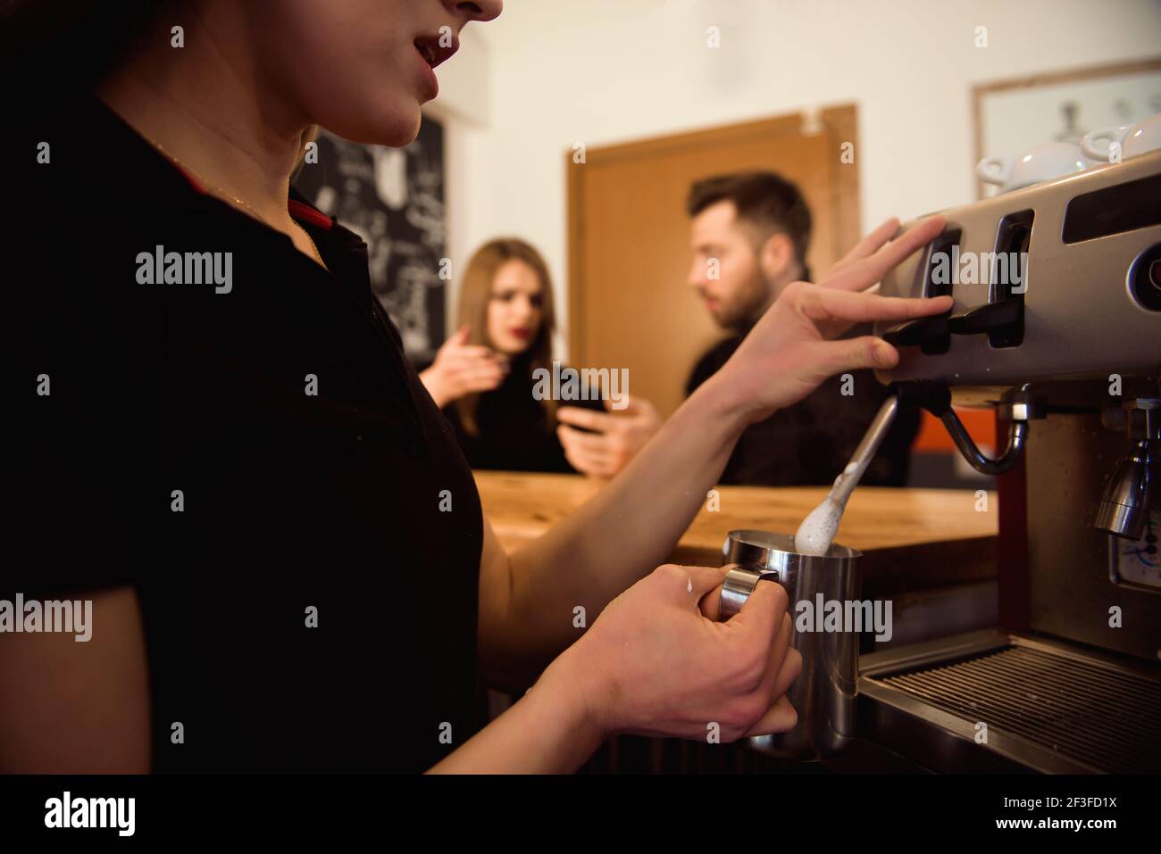 Professional female barista holding metal jug warming milk using the