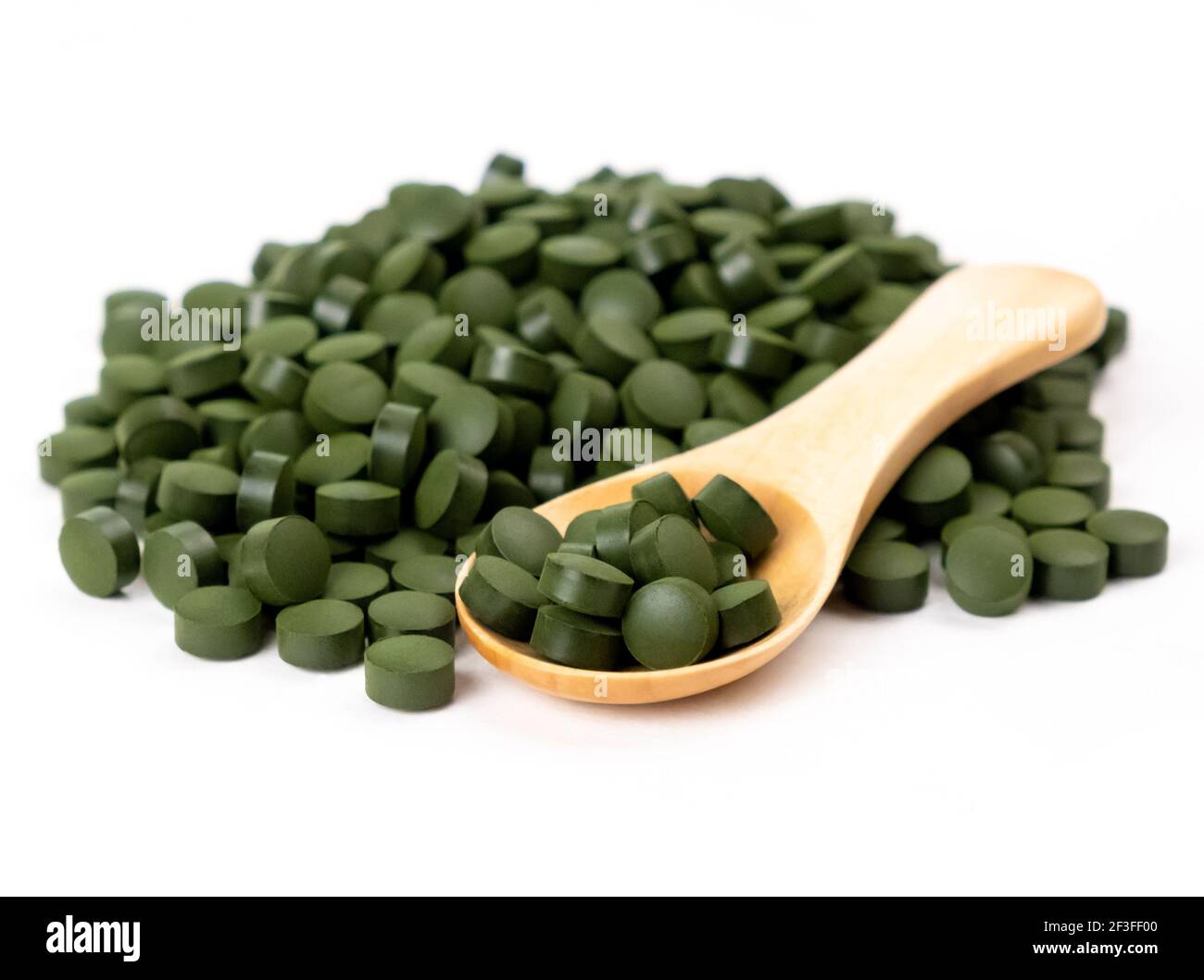 Spirulina algae tablets with a wooden spoon isolated on white
