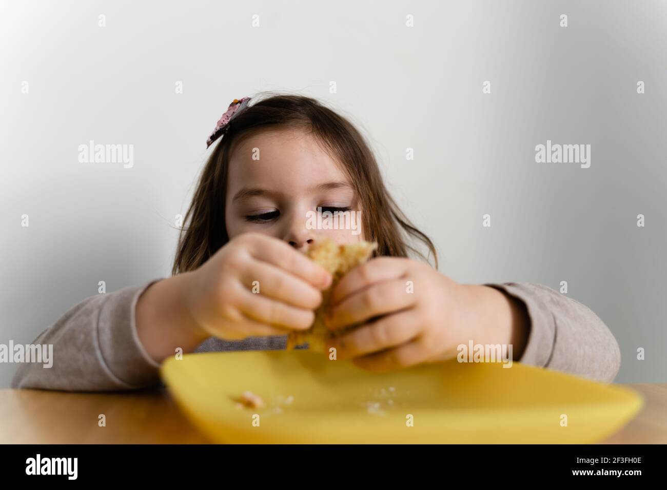 Toddler girl eating bread or pie at home with her hands. Hungry kid