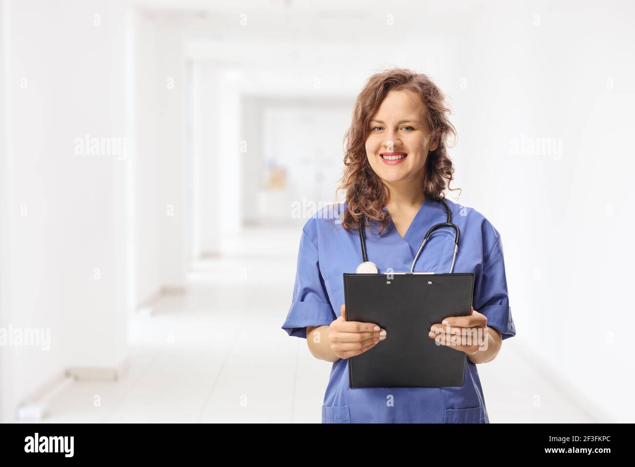 Young female intern in a blue uniform holding a clipboard in a hospital corridor Stock Photo