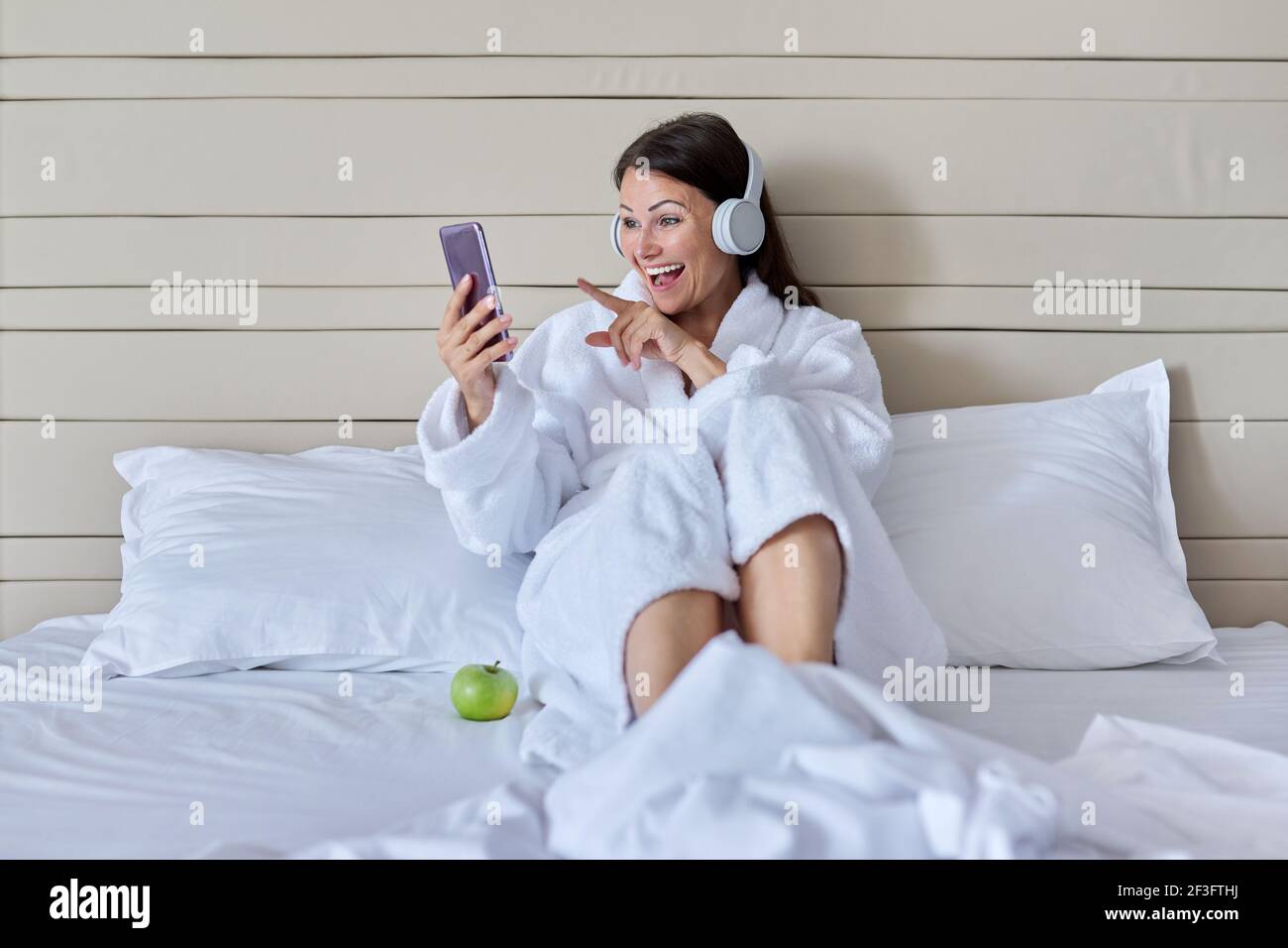 Happy talking mature woman in headphones using smartphone for video ...