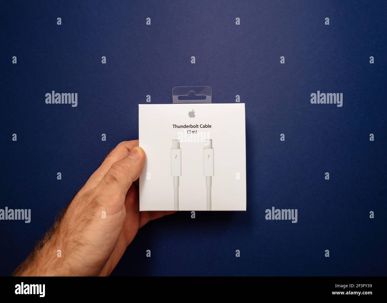 Overhead view of male hand holding Thunderbolt Cable 2 meter cable cardboard box manufactured by Apple Computers - isolated on blue background Stock Photo