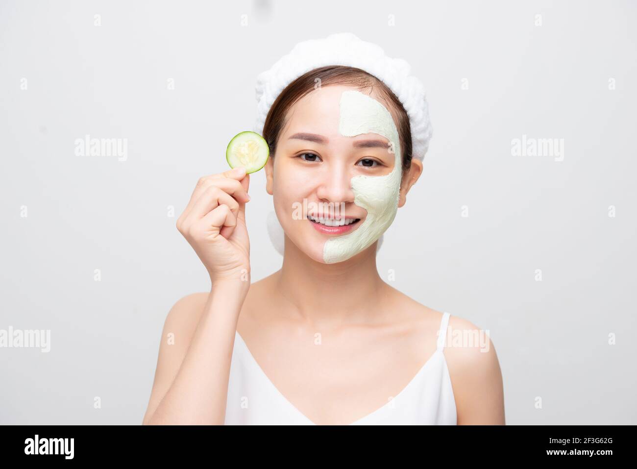 Attractive young Asian woman with clay mask and holding fruit piece isolated over white background. Beauty concept. Stock Photo