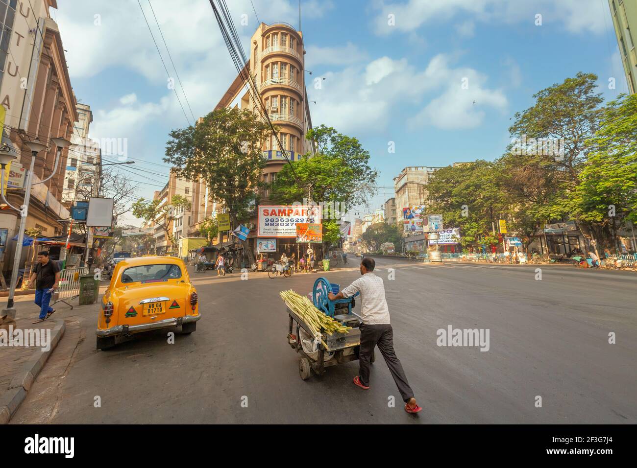 Vendor with a sugarcane juice cart on city road with view of office buildings at Chandni Chowk area of Kolkata, India Stock Photo