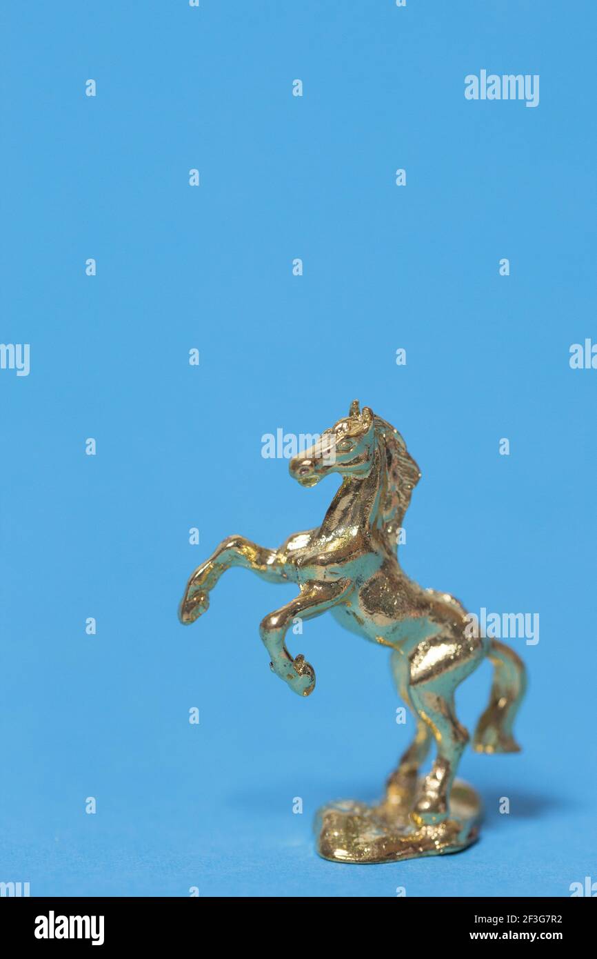A rearing gold horse toy figurine against a blue background. Stock Photo