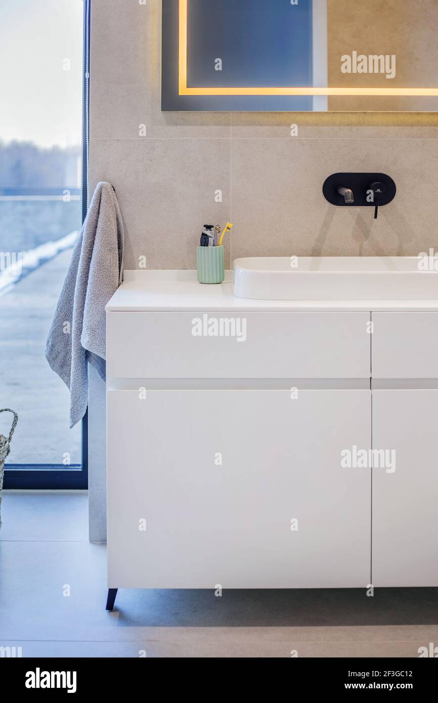Modern bathroom interior with a white sink on top of a white countertop and a mirror hanging above it. Stock Photo