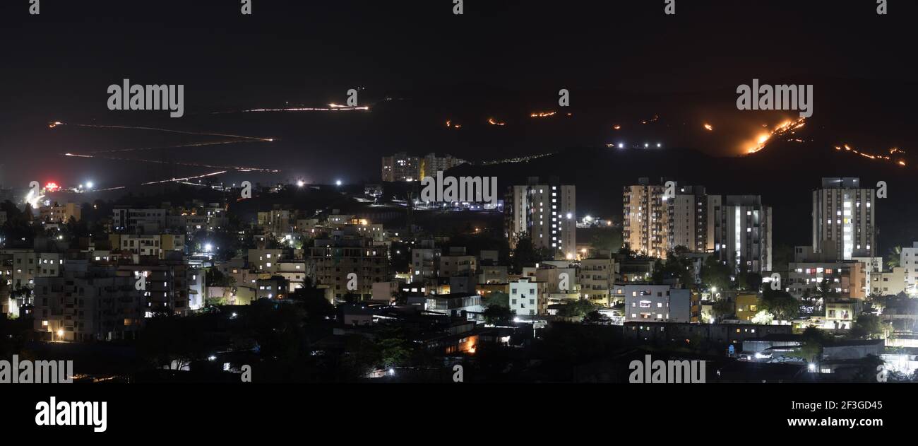 Night city view with light trails on the distant road and burning glass on another side, long exposure panorama. natural wildfire. Stock Photo