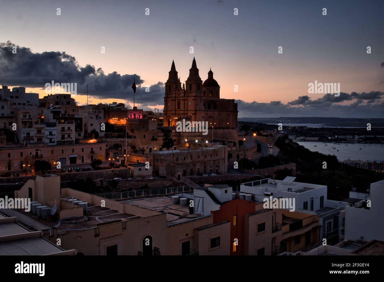 Historic white buildings and Parish Church in Mellieha, Malta lit up at night. Stock Photo