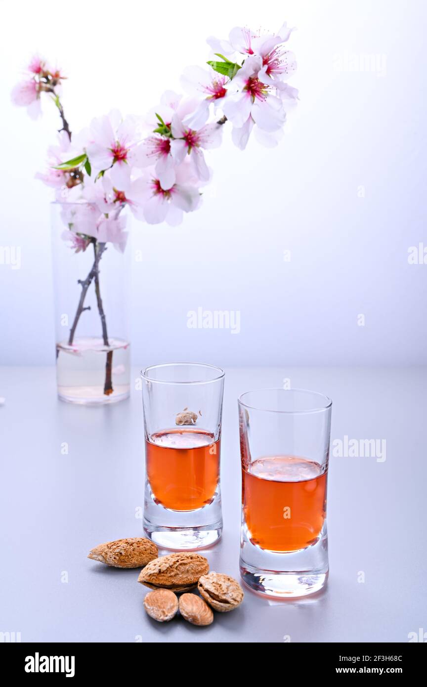 almond liquor. The traditional strong drink in italy to complete the dinner is a liqueur made from nuts and berries. Ratafia, alcohol in shot. on the table and a branch of blooming almonds. Copy space Stock Photo