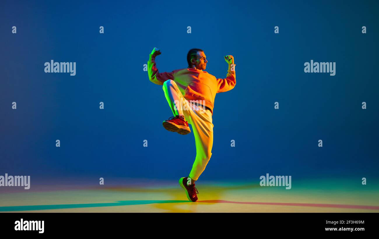 Young man dancing hip-hop in stylish attire on blue background in neon light Stock Photo