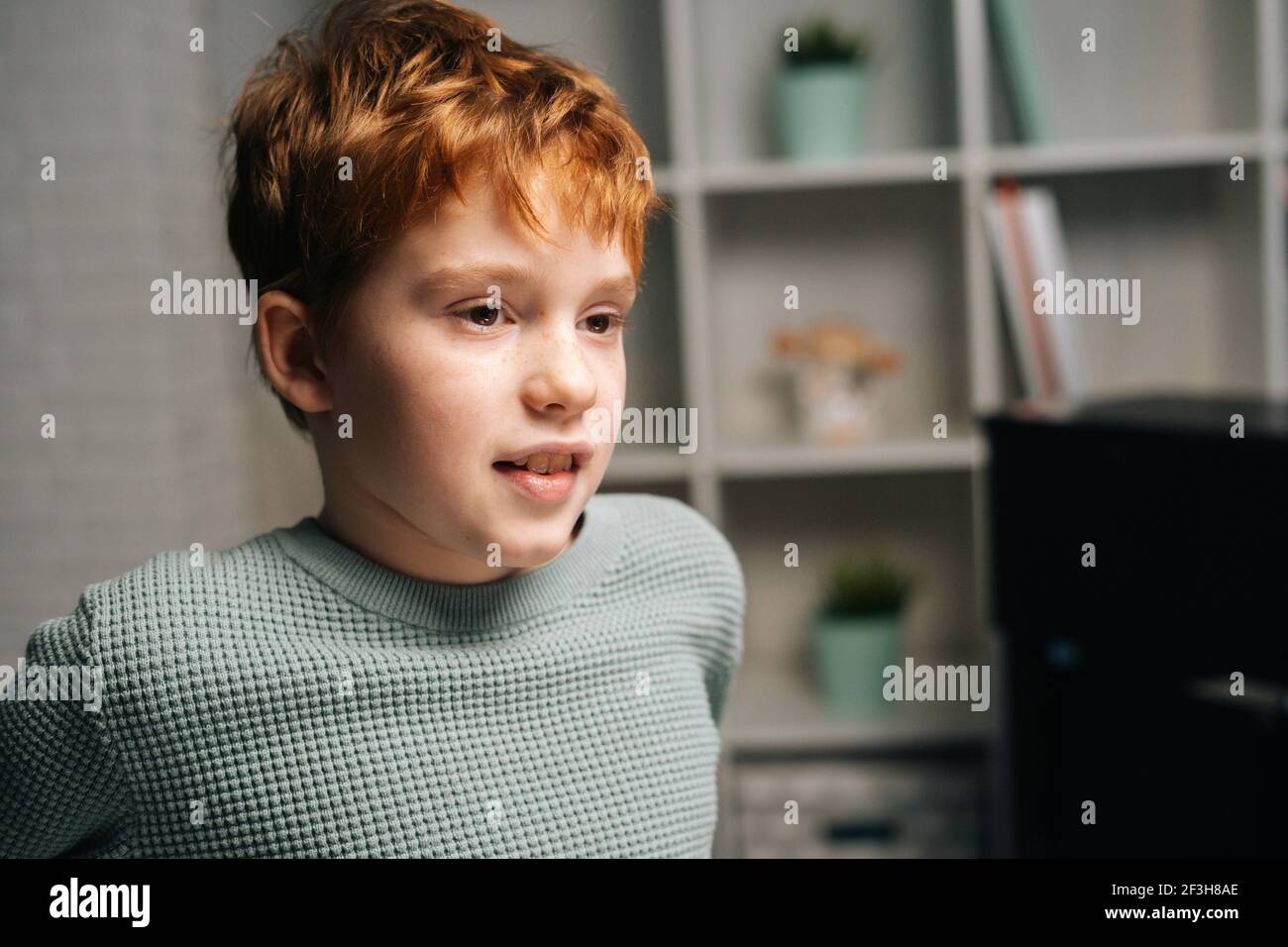 Close-up portrait of cheerful freckled redhead child boy sitting on table and looking away Stock Photo