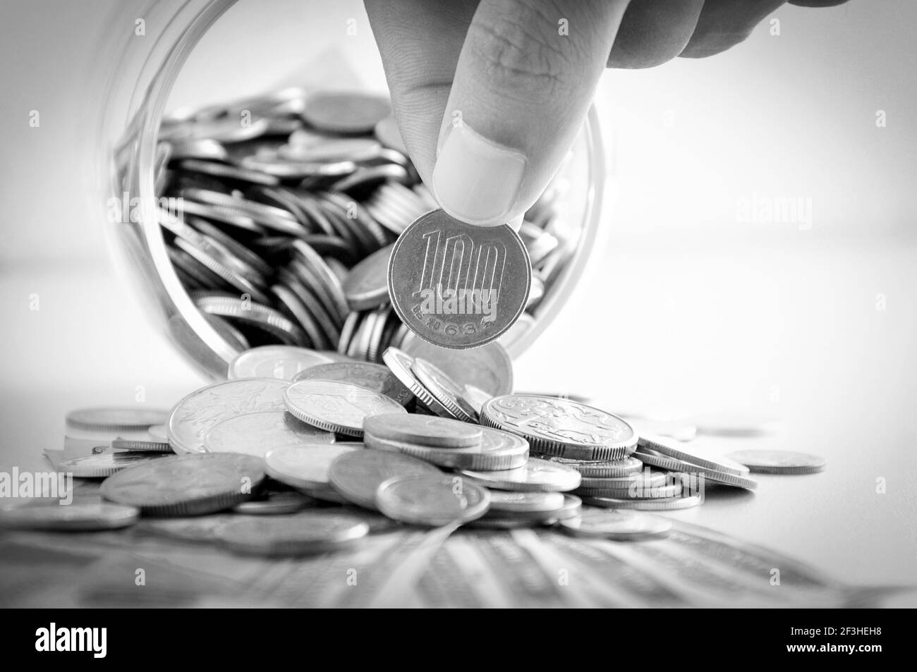 Hand picking up 100 Japanese yen (JPY) coin out of multi currency pile of coins - monochrome effect Stock Photo