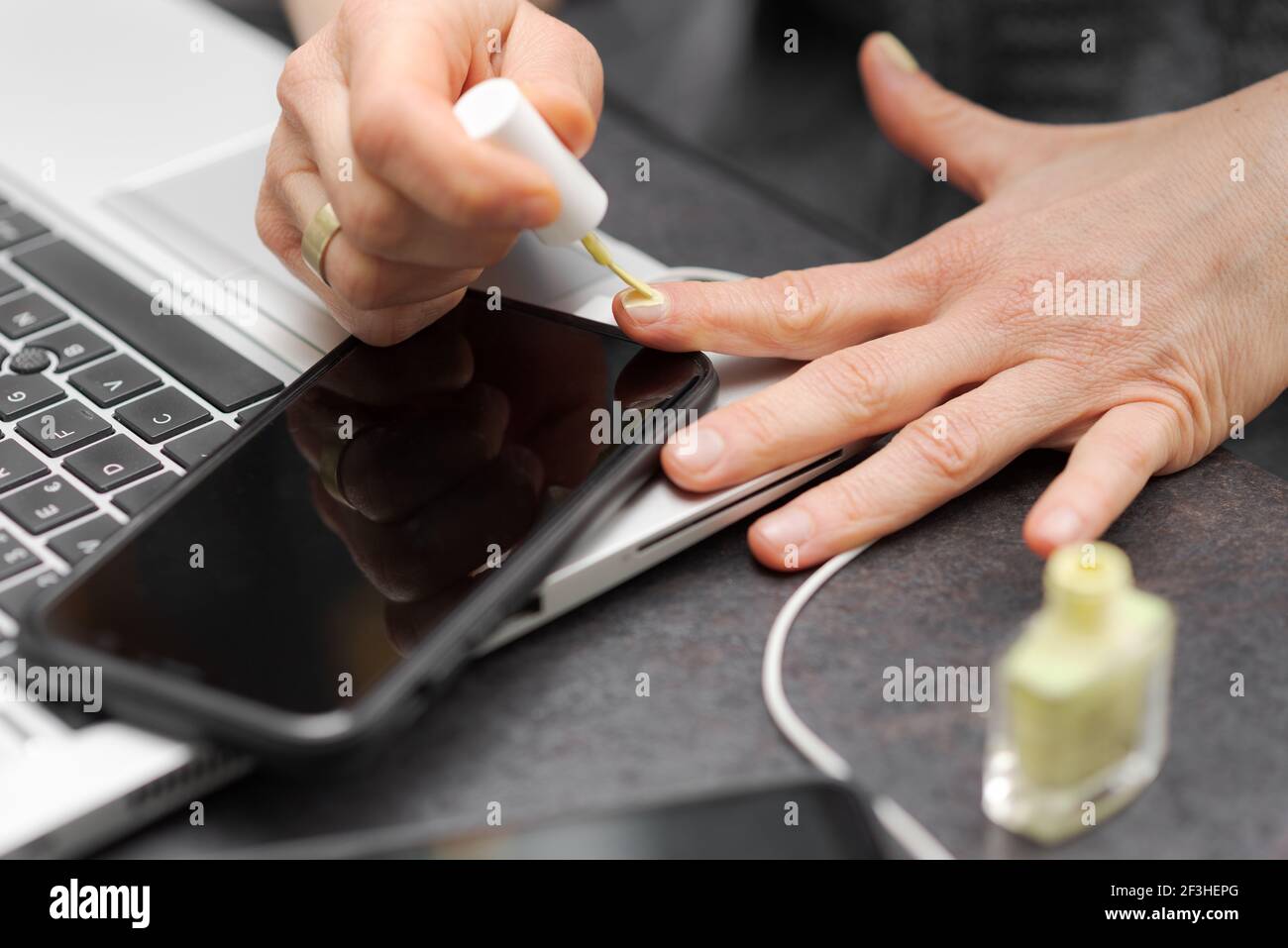 Female or male hands applying green nail polish on fingernails as stress relieve from work at desk in home office near laptop computer and smartphone Stock Photo