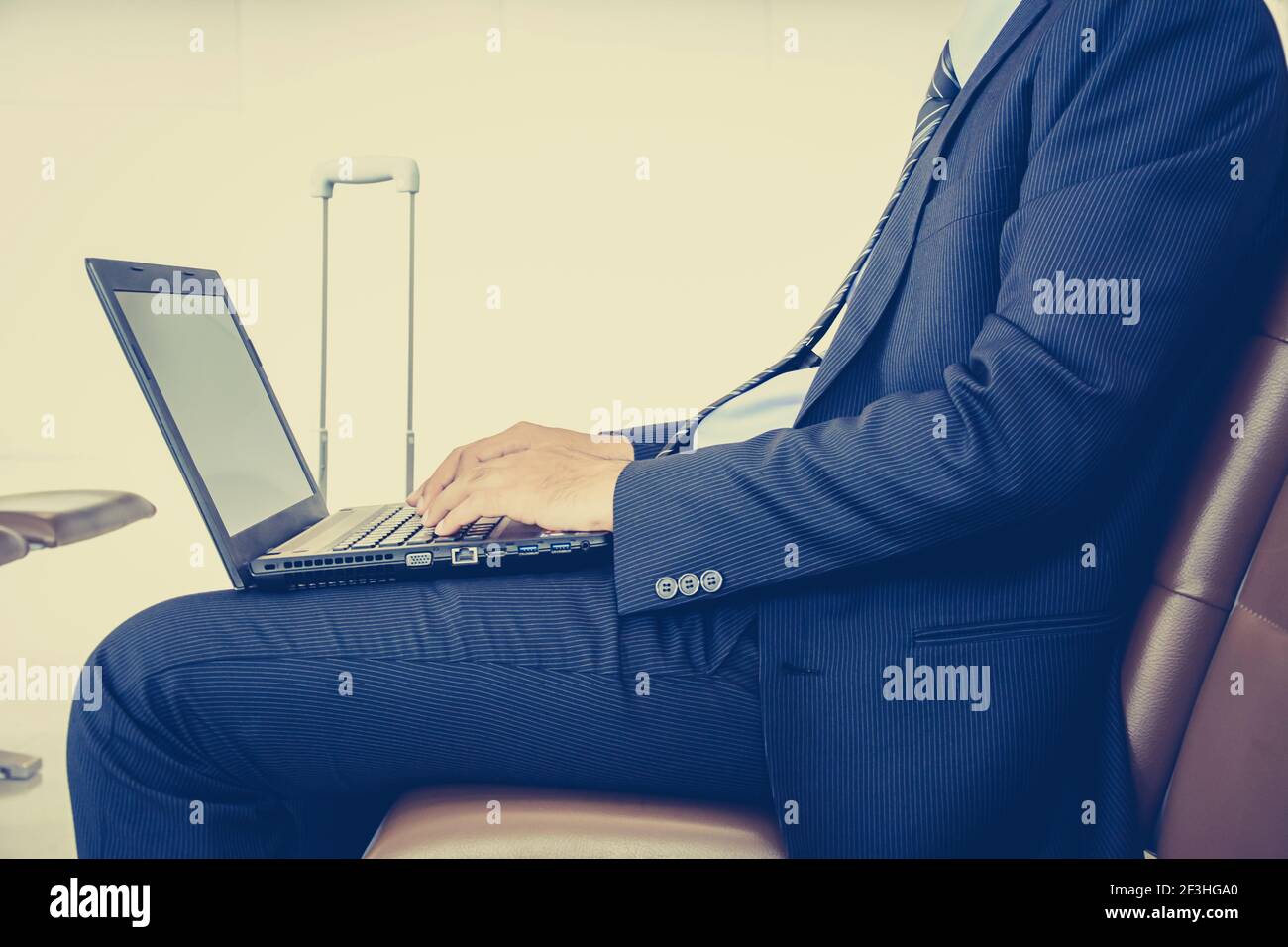 Businessman using laptop or notebook computer while sitting on the chair at the airport - vintage (retro) style color effect Stock Photo