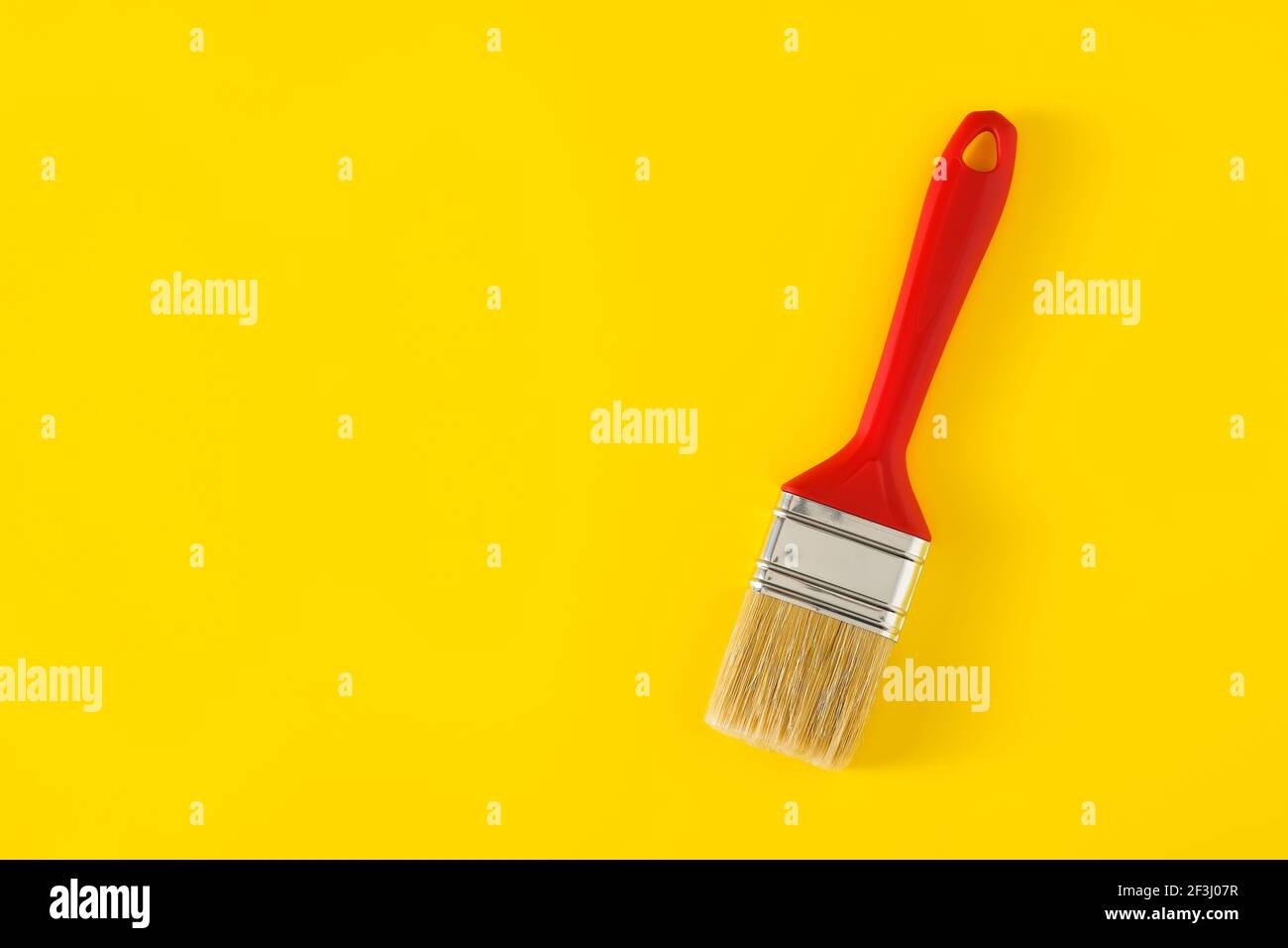 Paintbrush with red handle on yellow background. Stock Photo