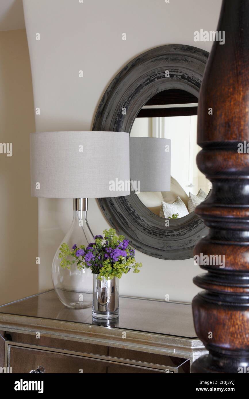 Lamp and flowers on mirrored chest of drawers in front of oval mirror | NONE | Stock Photo
