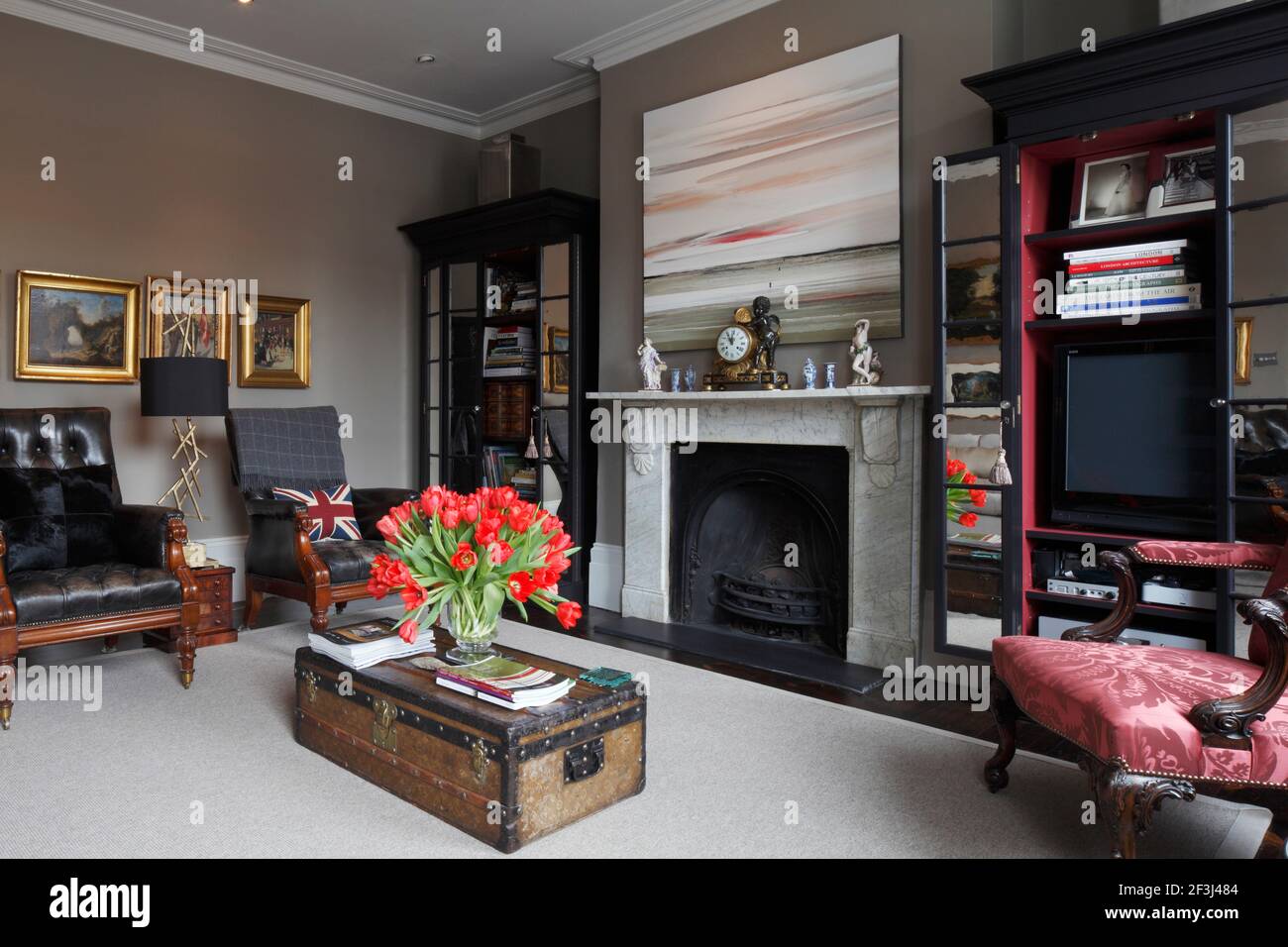 Salon avec cheminée en marbre, deux chaises à bouton de cuir noir et une  table basse Louis Vuitton vintage