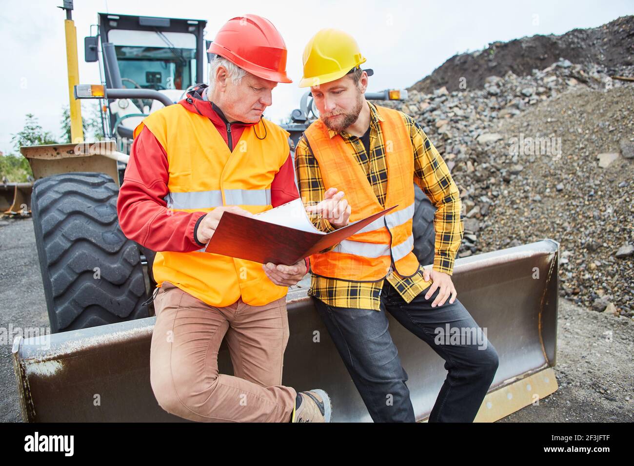 Two construction workers in front of a wheel loader when planning a house or road construction on a construction site Stock Photo