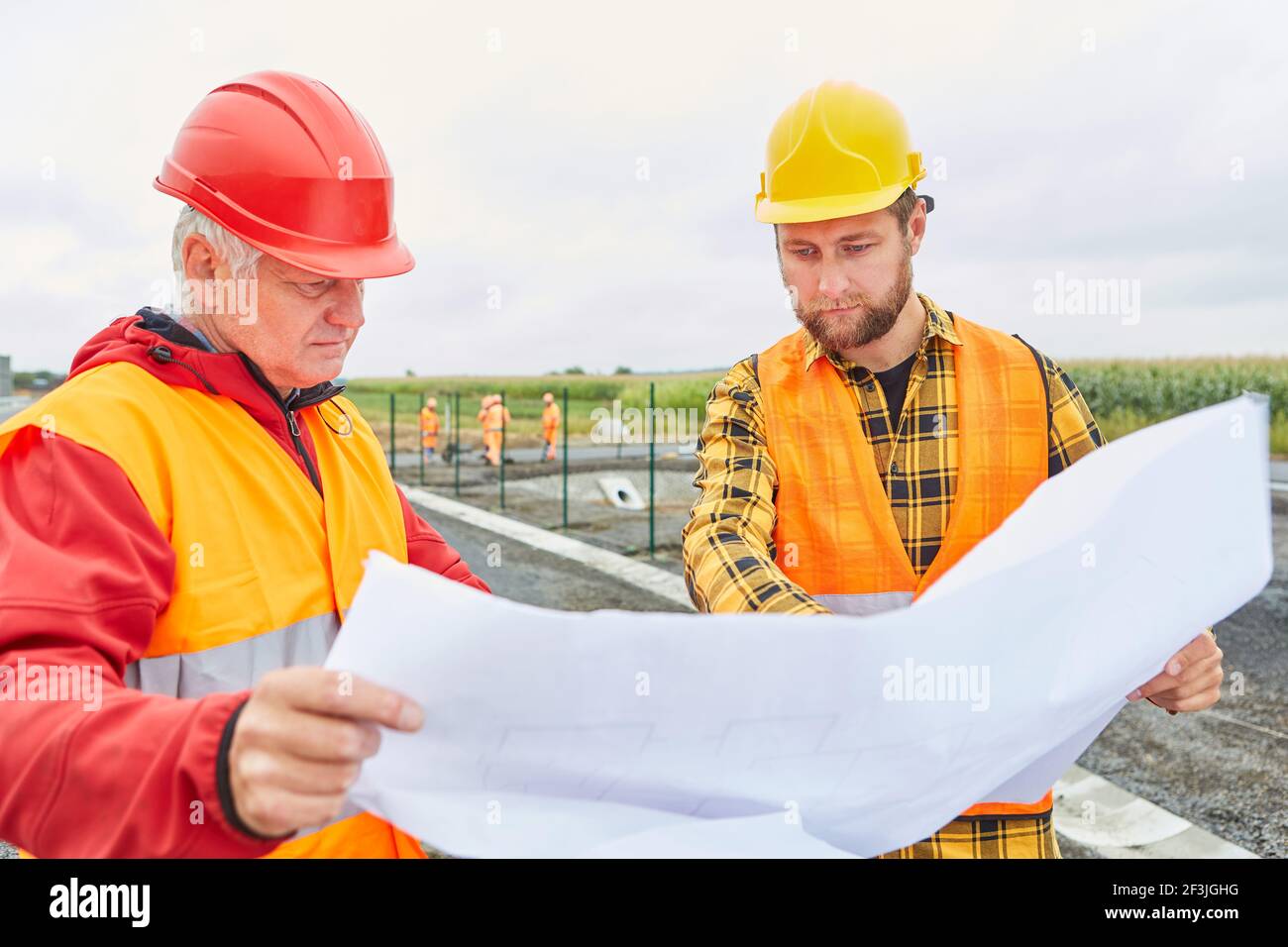 Two construction workers with site plan for house building and road construction project in the new development area Stock Photo