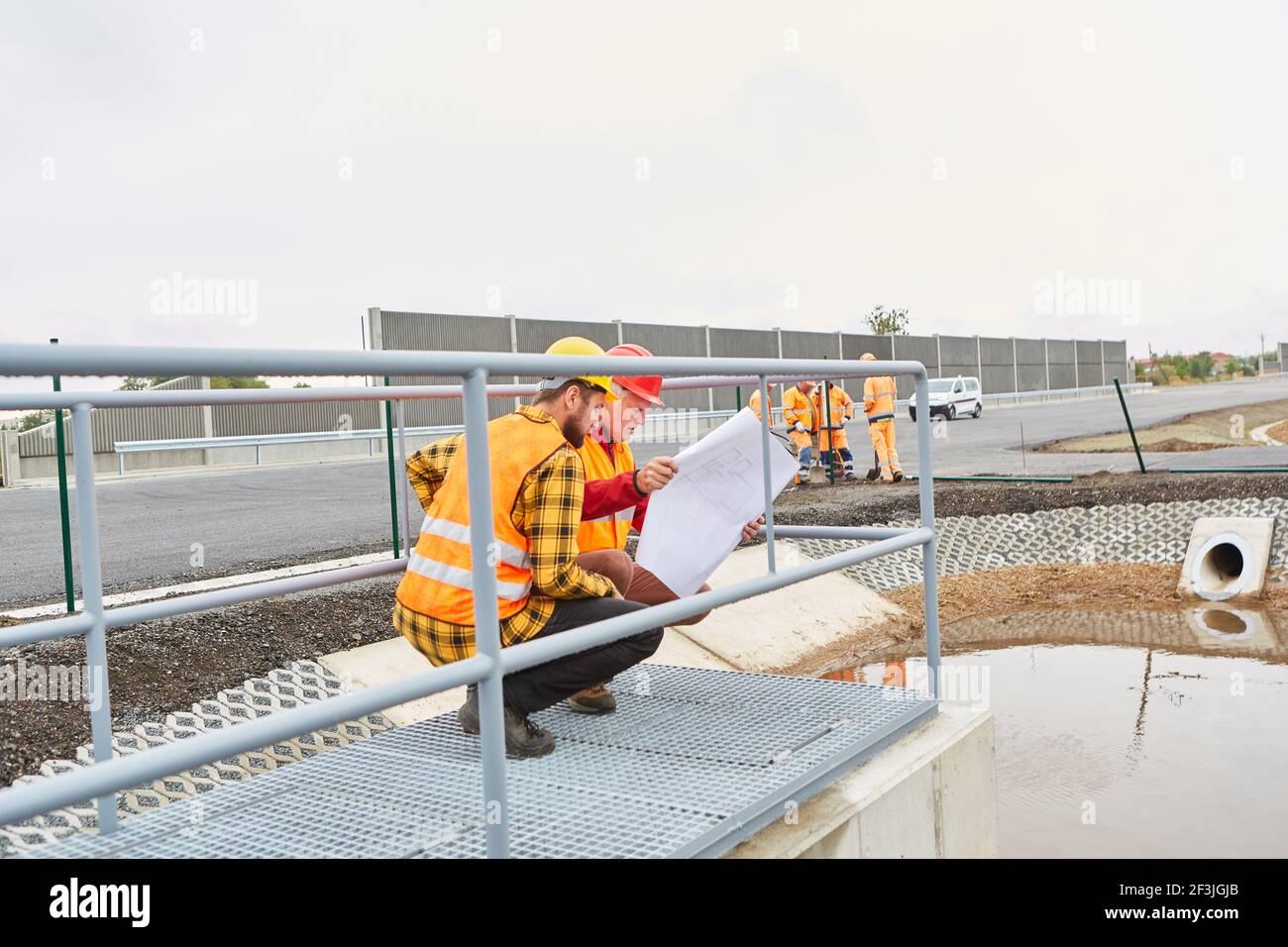 Two construction workers with plan control construction on the road construction site Stock Photo