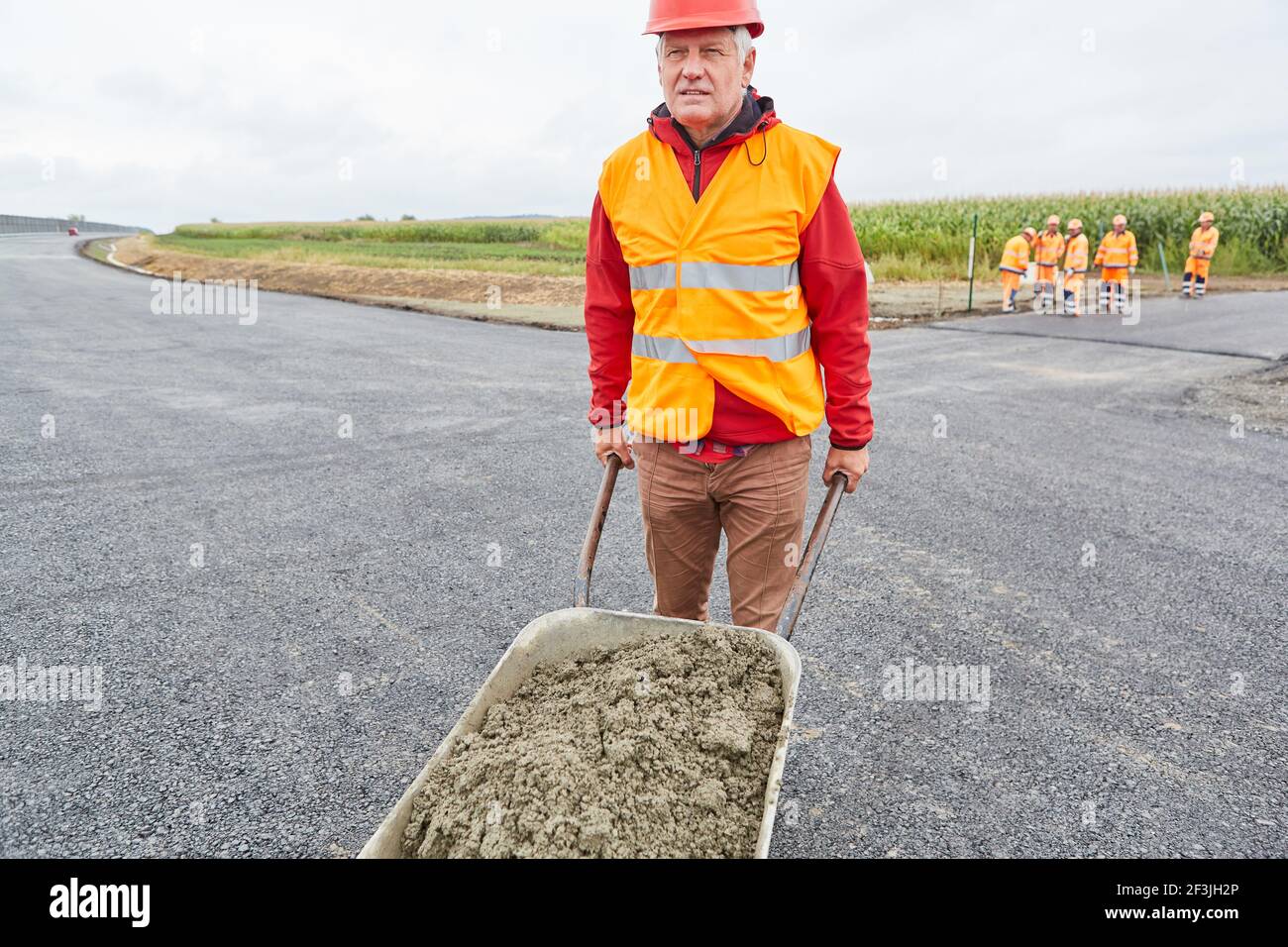 Construction worker pushes concrete in a wheelbarrow on road to ...