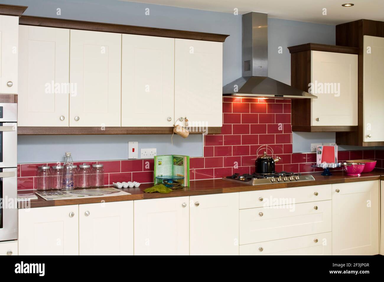 kitchen with red tiled wall and cream presses, hob and extractor fan