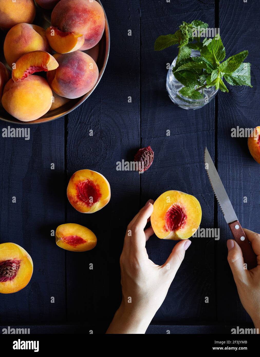 Woman cutting fresh juicy peaches and mint on the wooden table in the kitchen at country home Stock Photo