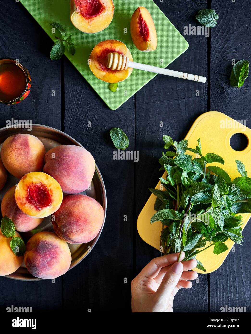 Woman holding fresh mint leaves near juicy peaches and honey on the wooden table in the kitchen at country home Stock Photo