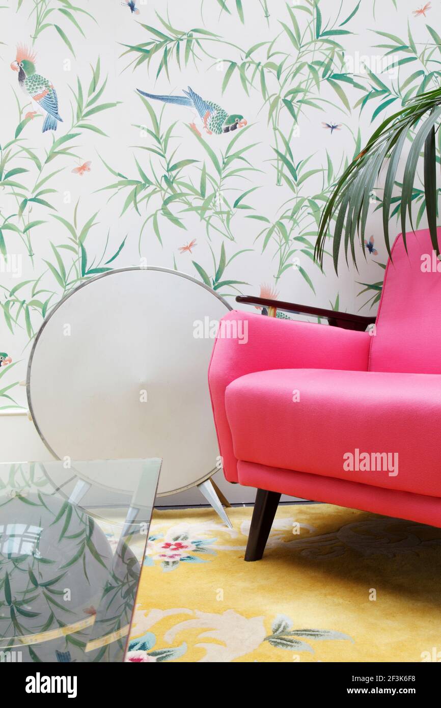 Mid century armchair in cersise fabric, and circular 50s electric heater against a wallpaper featuring bamboo and parrots |  | Designer: Shaun Clarkso Stock Photo