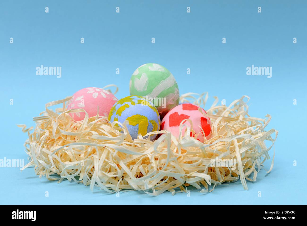 Children decorate colorful Easter eggs. Handmade nest with multi-colored eggs on a blue background. Easter, family, holiday and child concept. Stock Photo