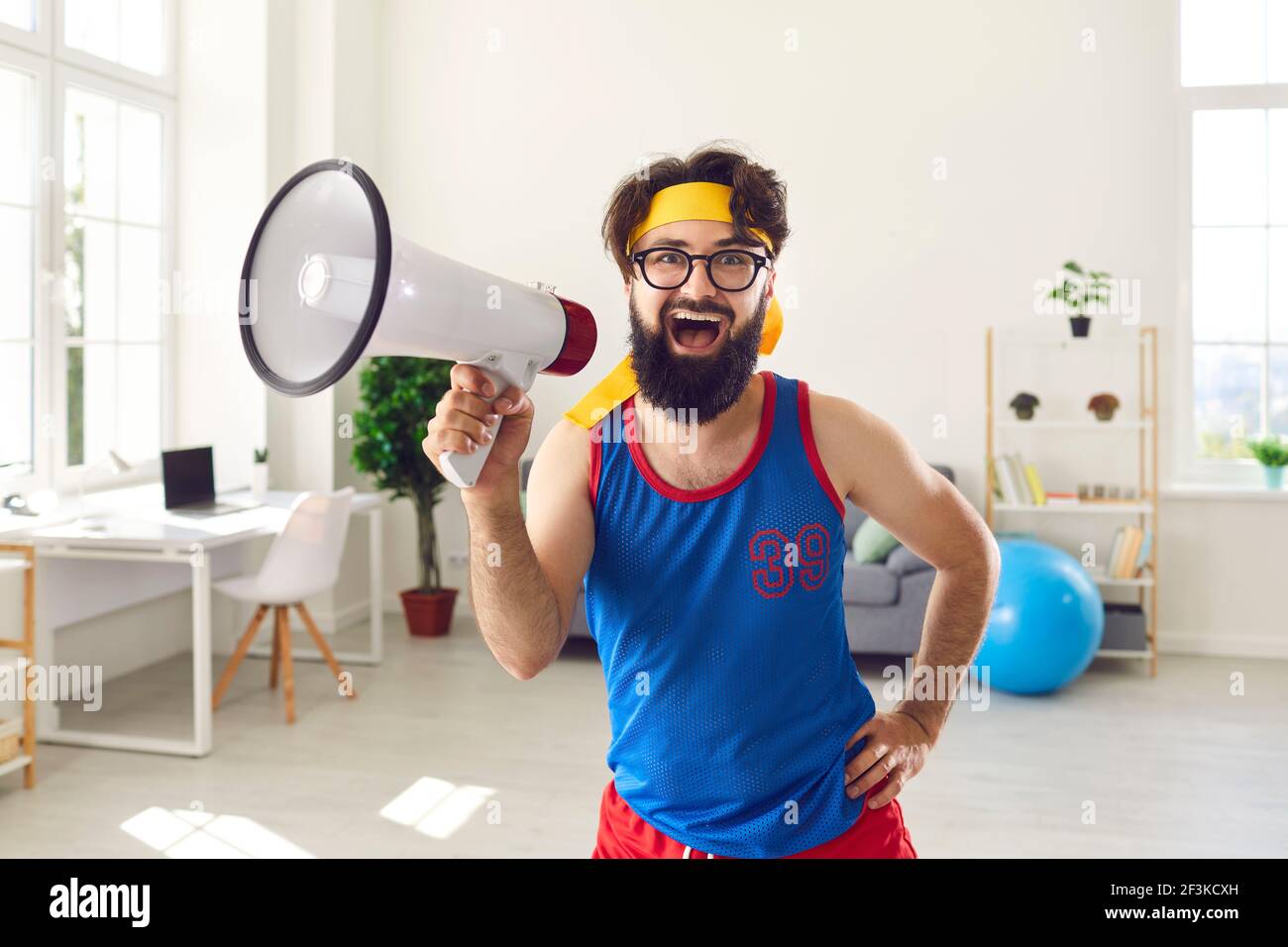 Athlete with a crazy expression is dressed in bright comic clothes shouting into a loudspeaker. Stock Photo
