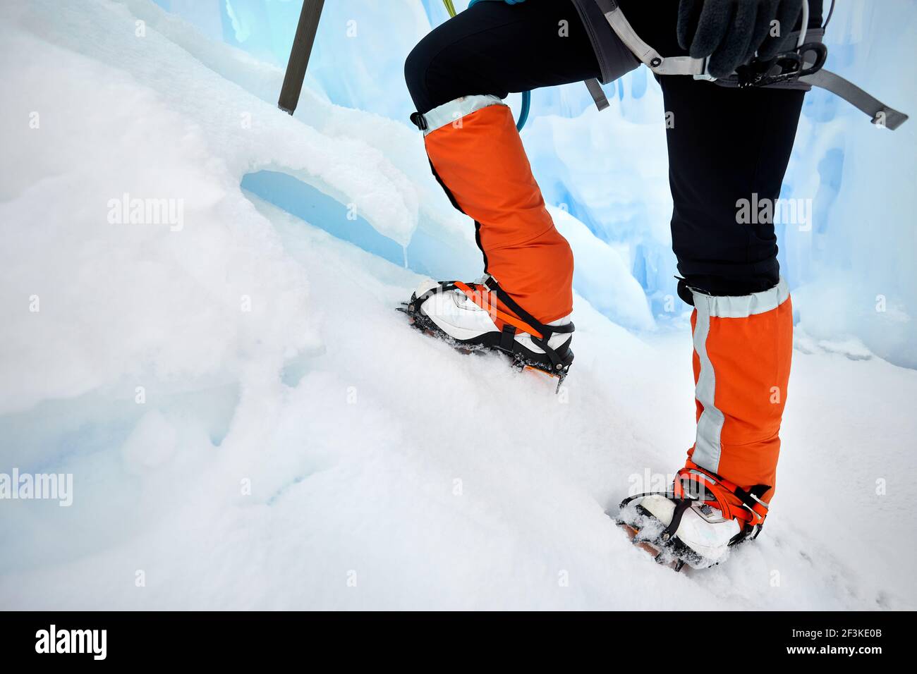 Woman climber in orange gaiters with ice axe near frozen waterfall in the mountains in Almaty, Kazakhstan Stock Photo