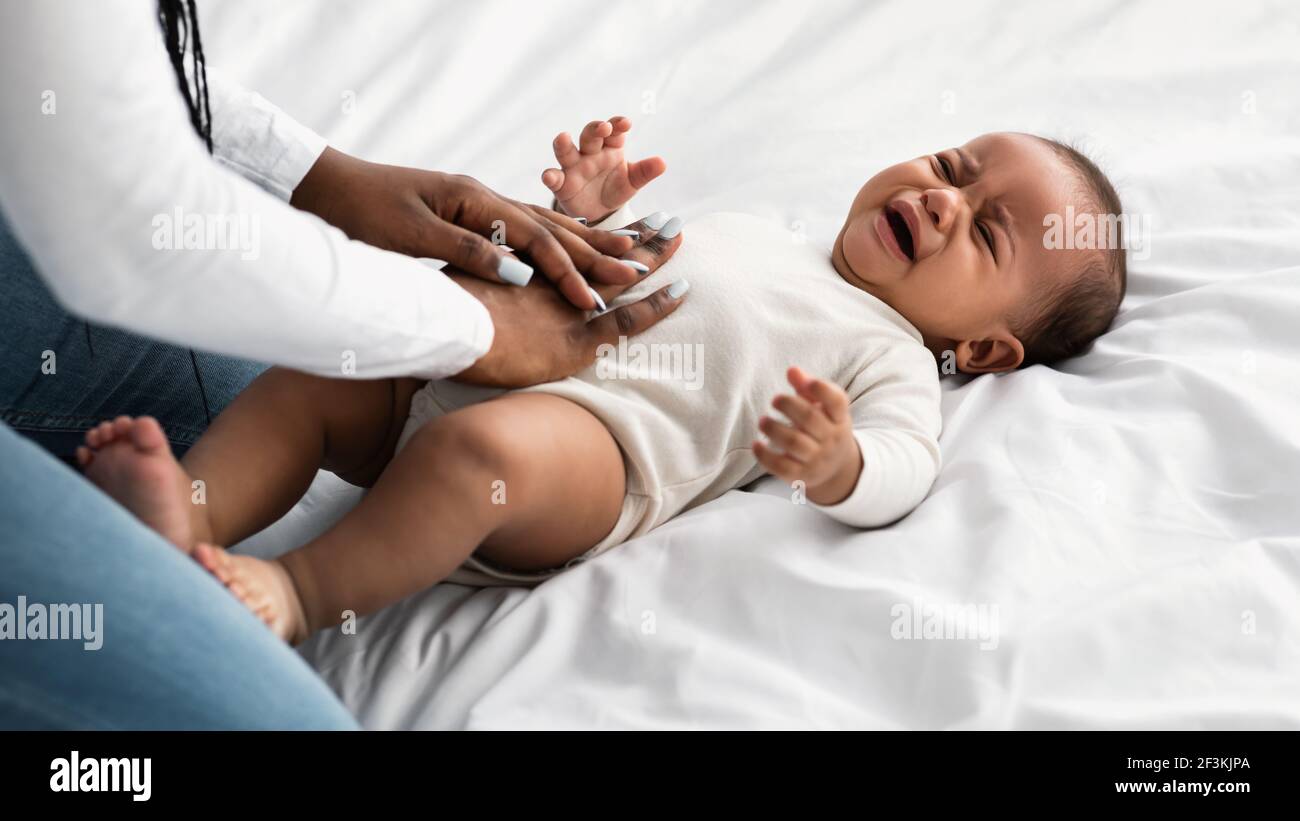 Portrait of black mother doing belly massage for crying baby Stock Photo