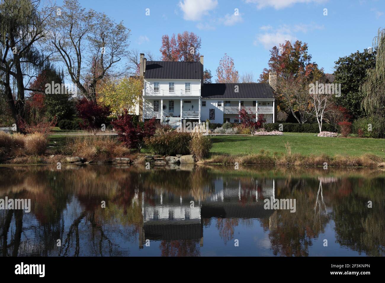 Colonial home with porches and lawn and pond in the foreground. Autumn ...