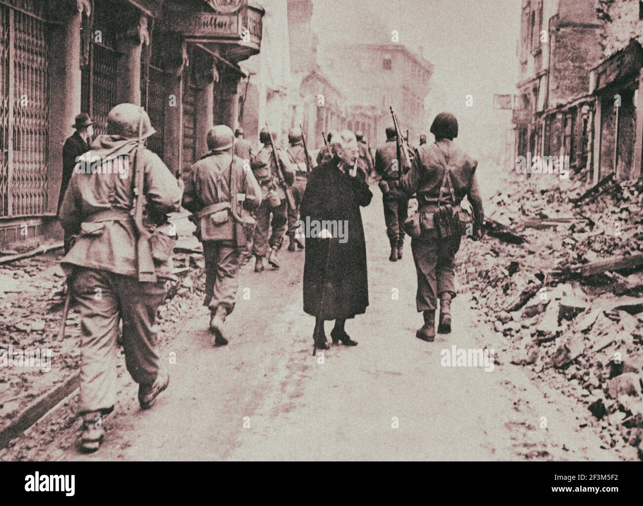 Archival photo of elderly woman views damage as American soldiers advance. Germany. 1945 Stock Photo