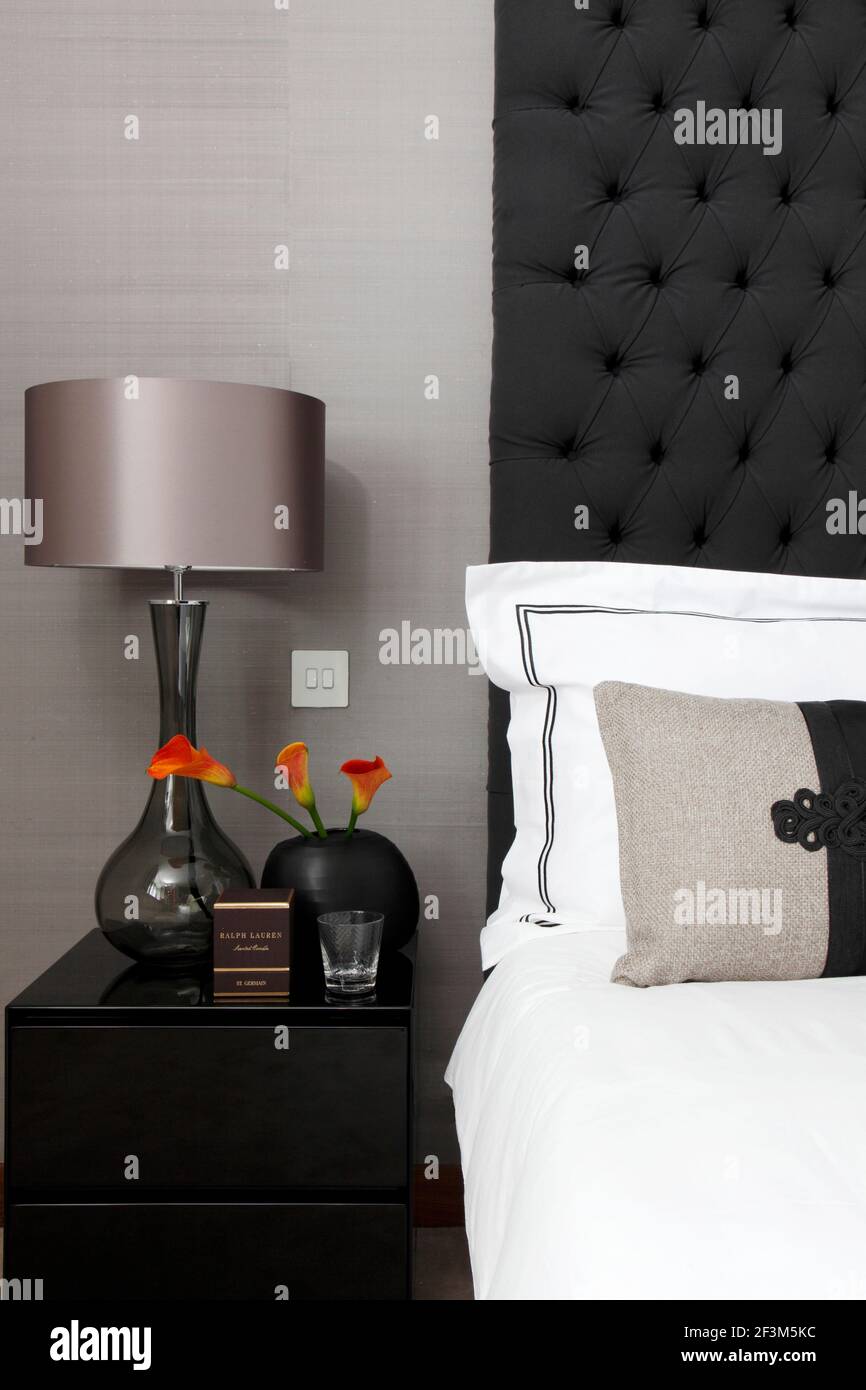 Detail of bed and bedside table, with glass lamp and silk shade, vase of  orange Arum lilies against neutral wallcovering in UK show home Stock Photo  - Alamy