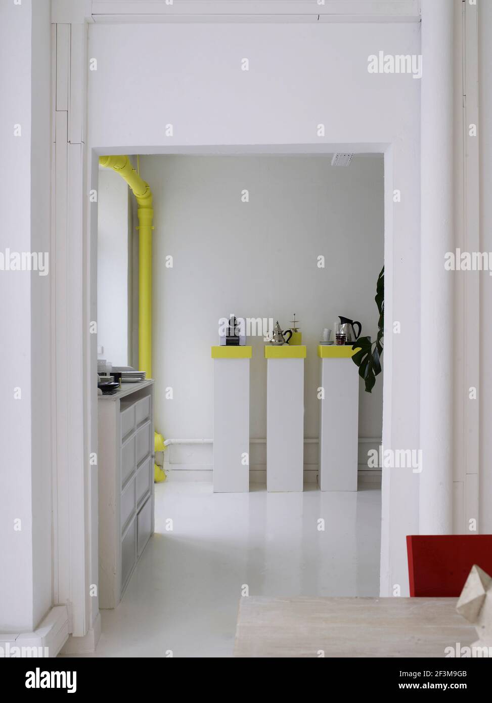 Entrance to modern kitchen with fluorescent pipe and kitchenware on top of rectangular stands in French residential home. Stock Photo