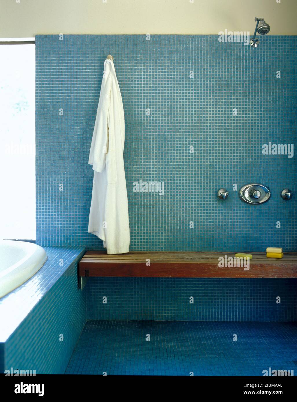 Blue tiled bathroom with wooden bench and shower with hanging bathrobe