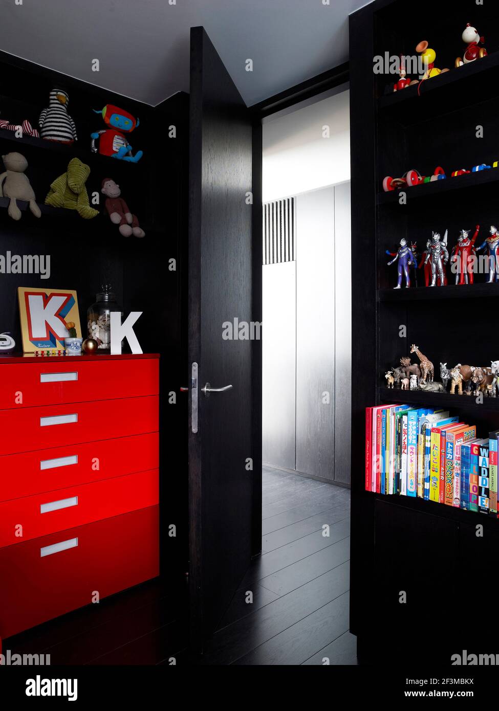 Bedroom with black walls, door and floor, with colourful toys and books on shelves and a bright red set of drawers in residential home, UK. Stock Photo