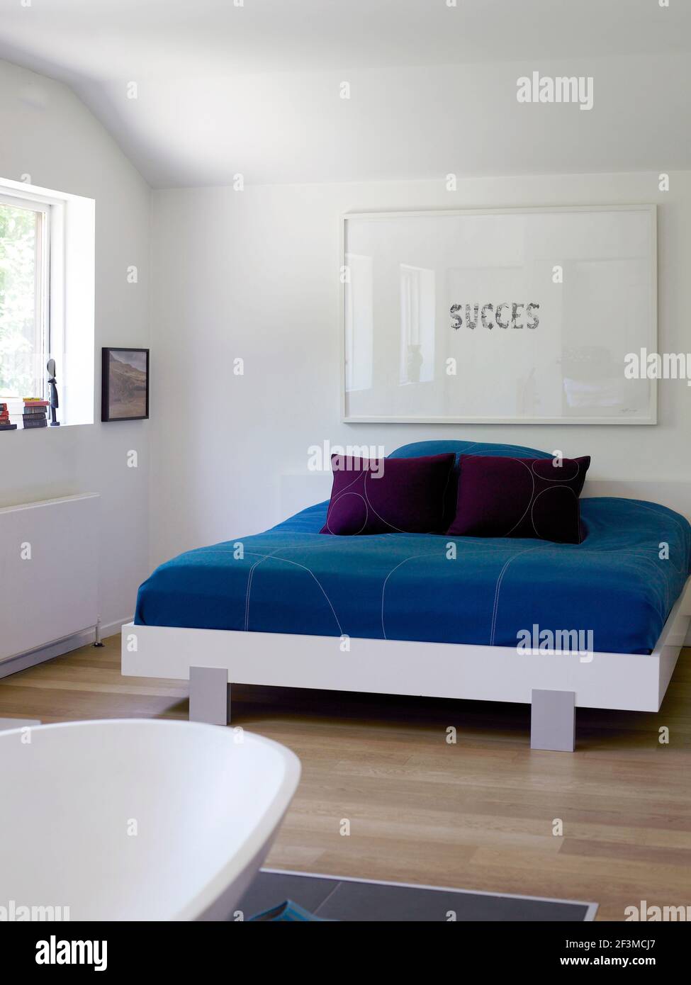 Blue bedcovers under artwork reading 'success' in bedroom of residential house, Denmark. Stock Photo