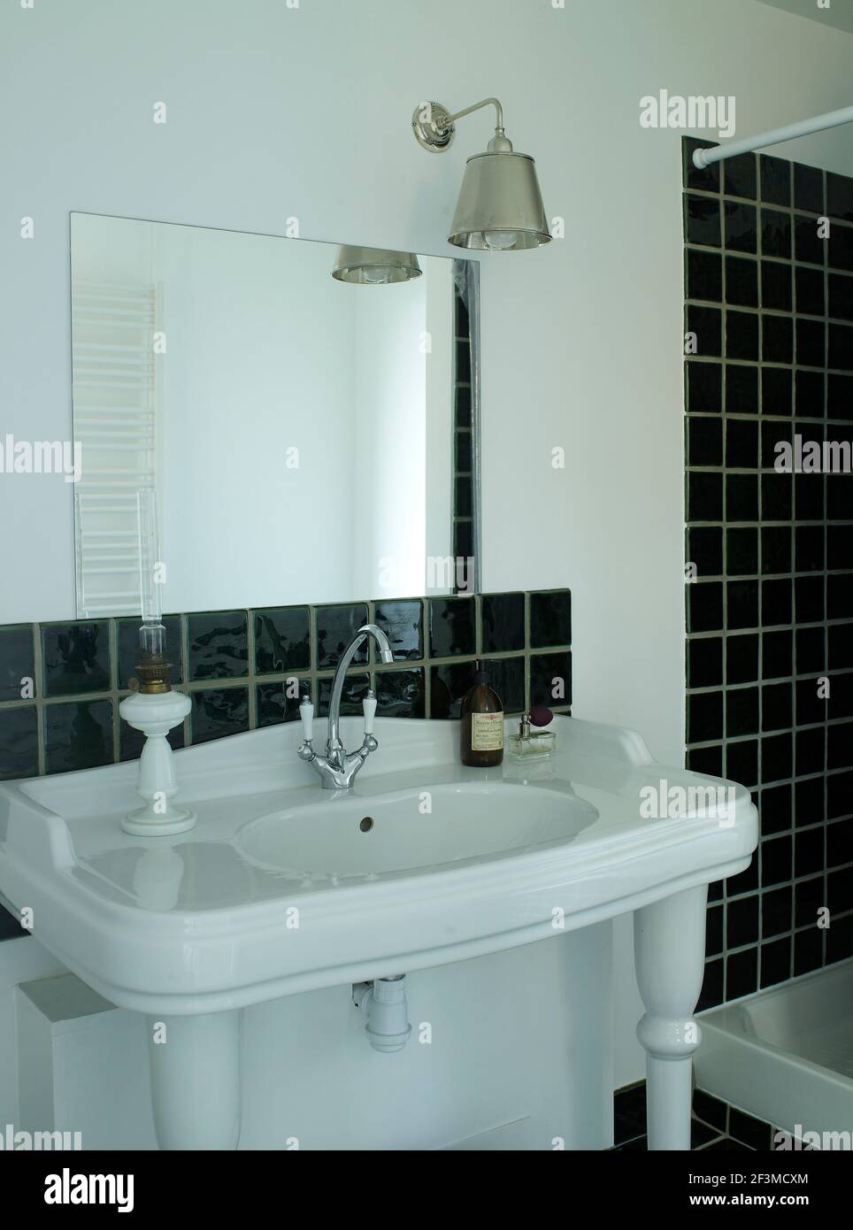 Black tiled splash back with large wash basin, pendant lamp and mirror of bathroom in residential house, France. Stock Photo