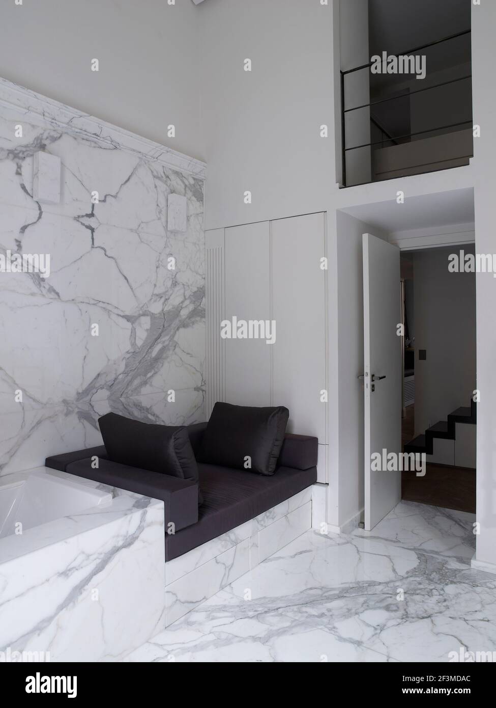 Marble bathroom with soft cushioned seating with view through open door to stairs and split level balcony in residential house, France. Stock Photo