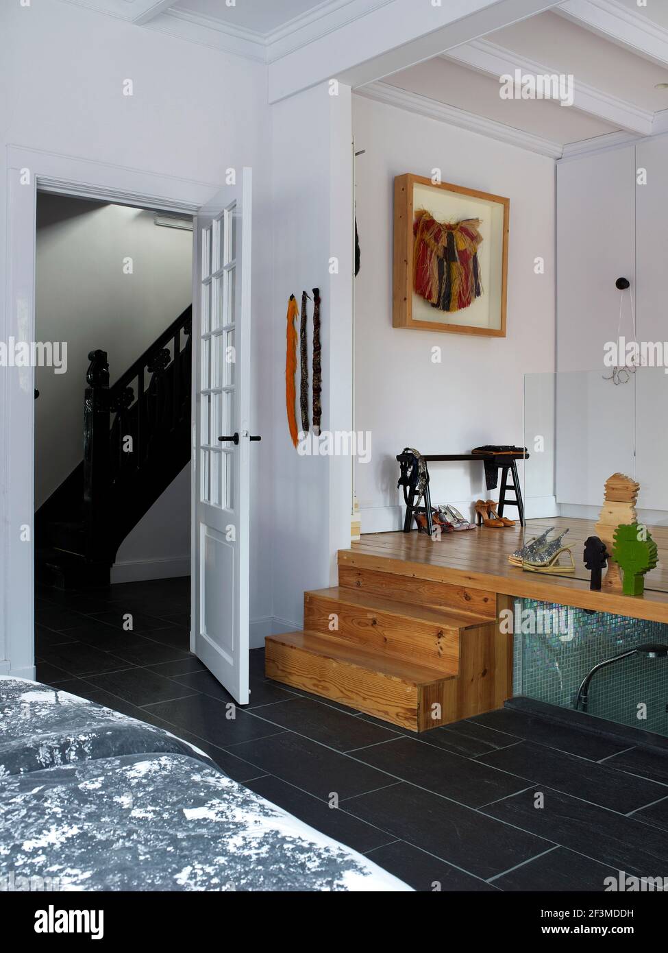 Split level small space living area with transparent panel with view to bathroom and doorway with view through to staircase with artwork in residentia Stock Photo