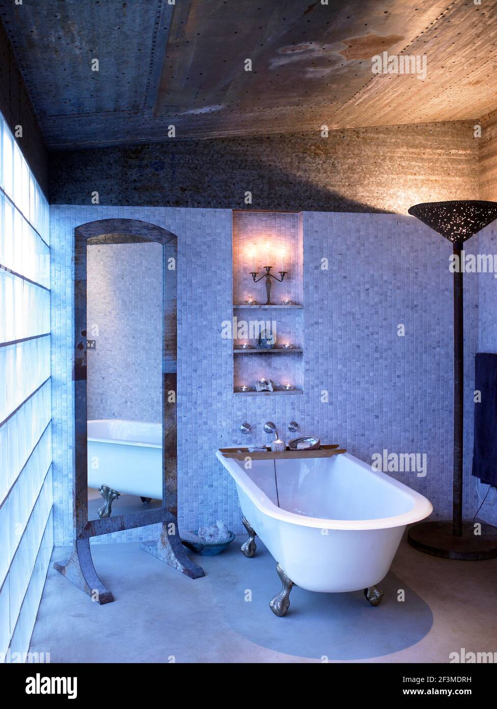 Glass wall in bathroom with free standing bathtub, full length standing mirror and large up lighting standard lamp in residential house, Australia. Stock Photo