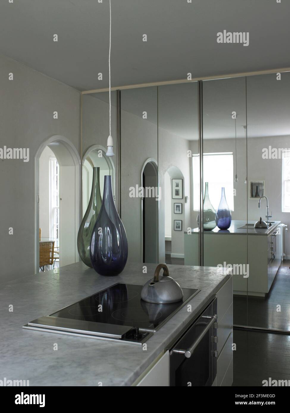 Island unit with kettle and glass necked vases in kitchen with mirrored wall in residential house, Australia Stock Photo