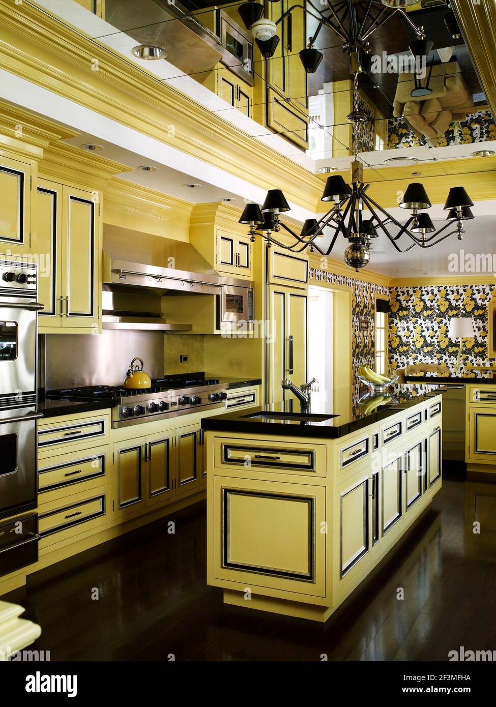 Chandelier hanging from mirrored ceiling above island unit in yellow and black kitchen in residential home, California, USA Stock Photo